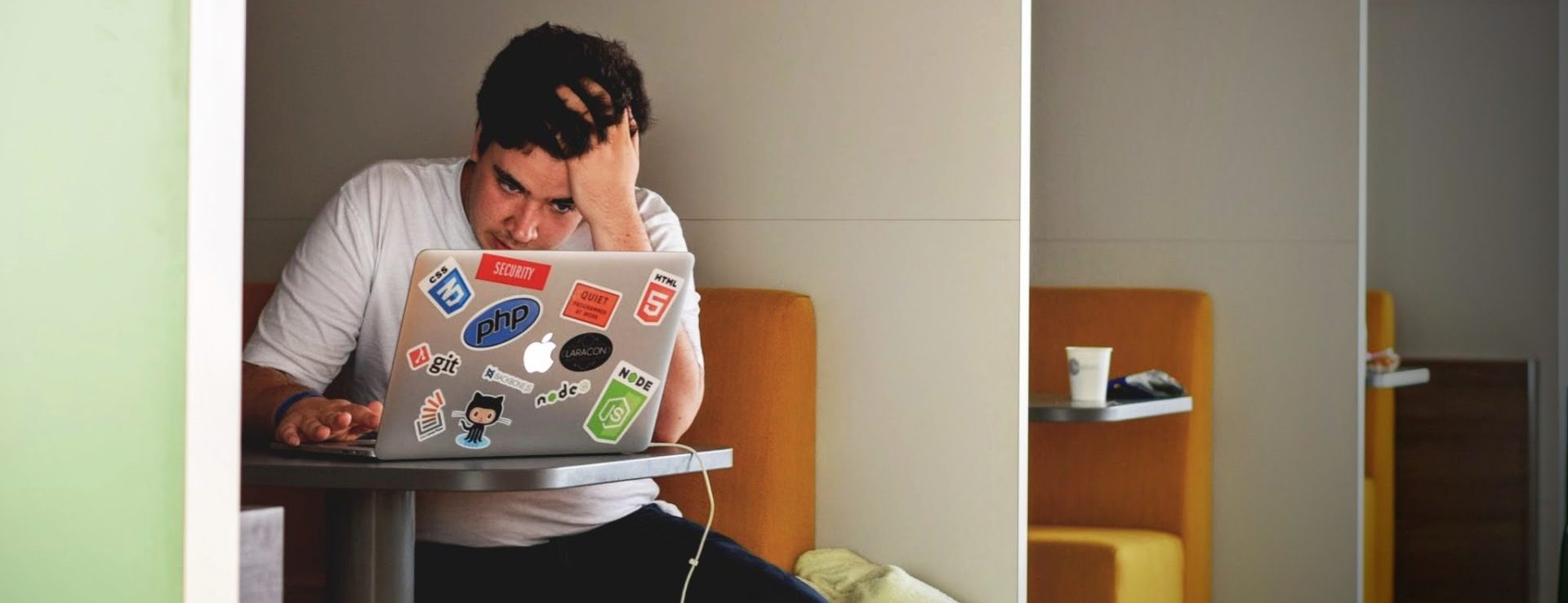 Mannlig student drar seg i håret mens han ser ned på en dataskjerm.