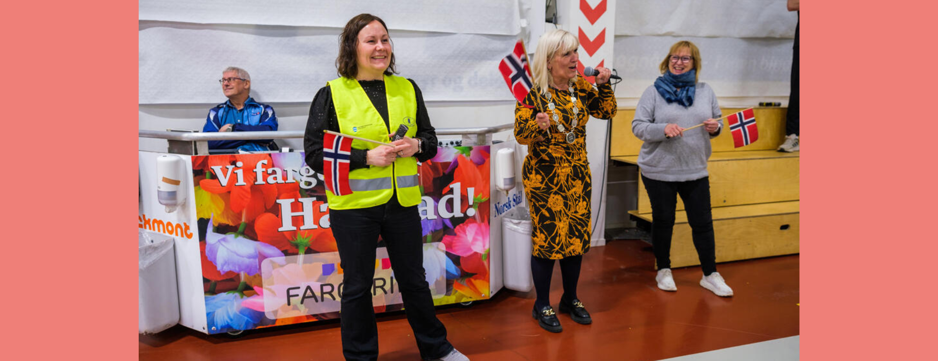 Dame med refleksvest og norsk flagg som står og ser utover salen.
